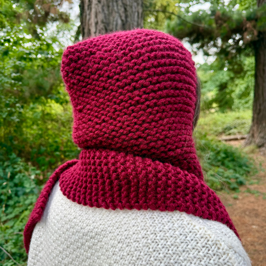 Person wearing a red knitted hood in a forest setting
