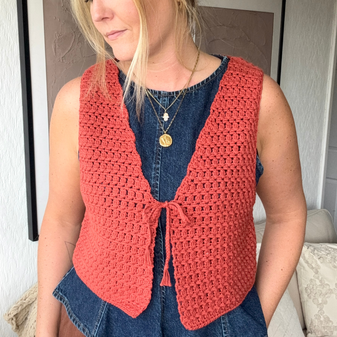 Person wearing a red crochet vest over a denim dress indoors.