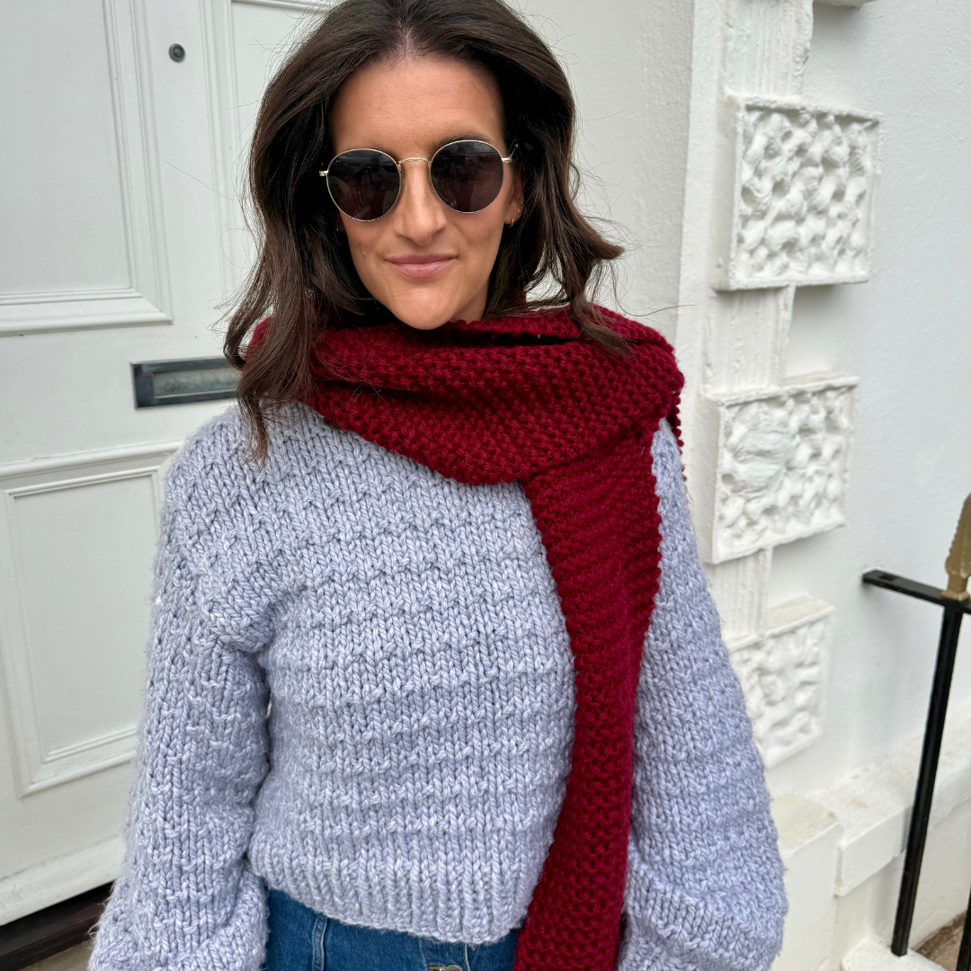 Woman wearing a red scarf and sunglasses in front of a white door.