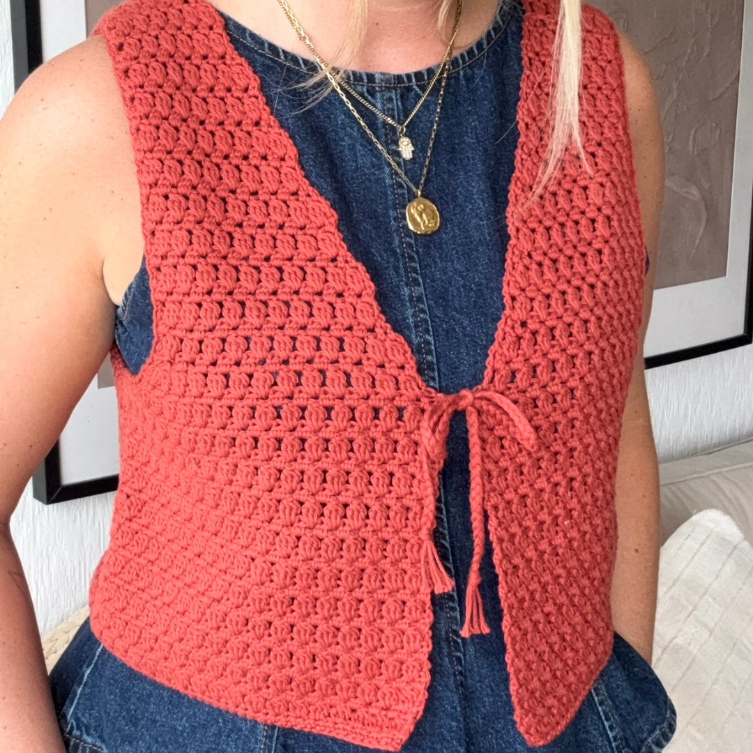 Person wearing a red crochet vest over a blue denim shirt.