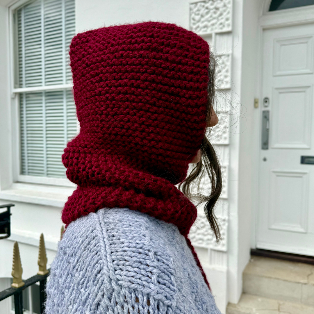 Person wearing a red knitted hood in front of a white door.