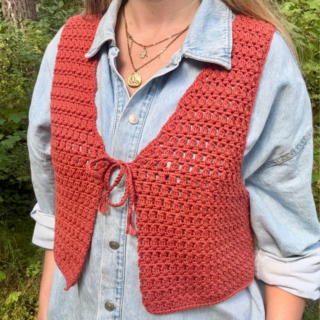 Person wearing a red crochet vest over a light blue denim shirt in a forest setting