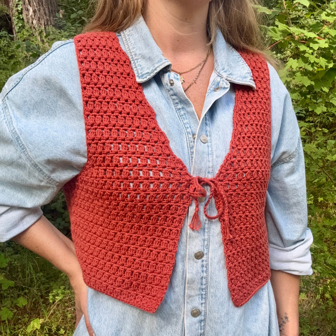 Person wearing a red crochet vest over a light blue denim shirt in a forest setting