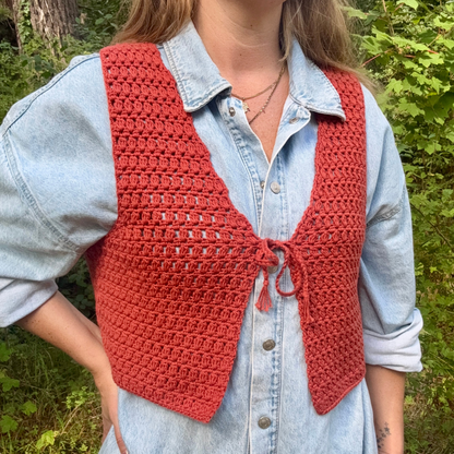 Person wearing a red crochet vest over a light blue denim shirt in a forest setting