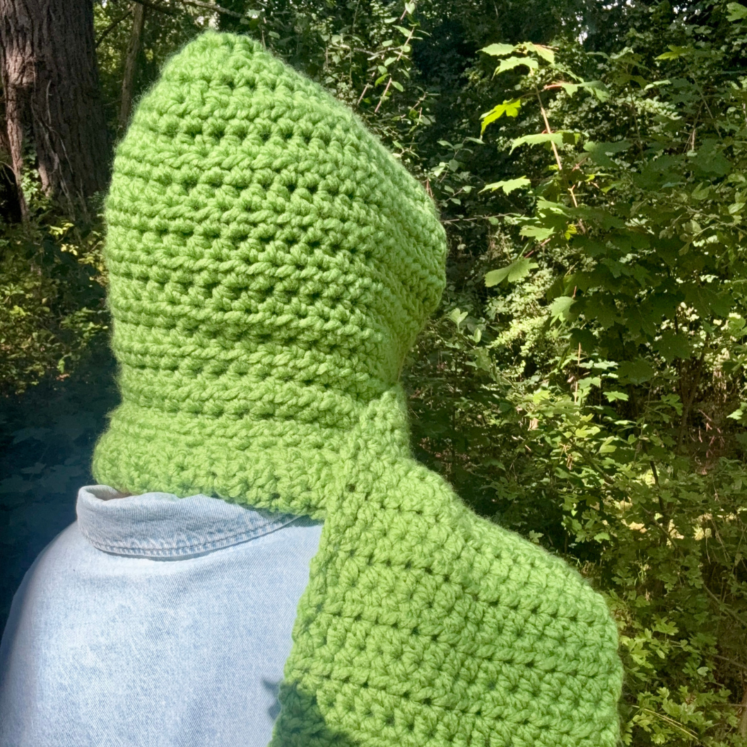 Green crochet hood worn by a person in a forest setting