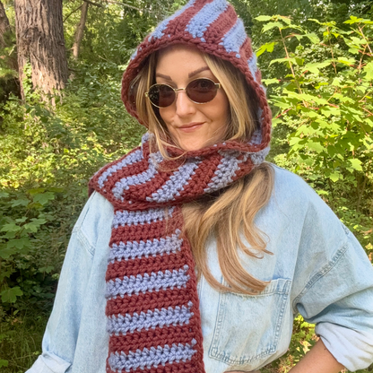 Person wearing a striped crochet hood and scarf in a forest setting