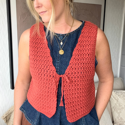 Person wearing a red crochet vest over a denim dress indoors.
