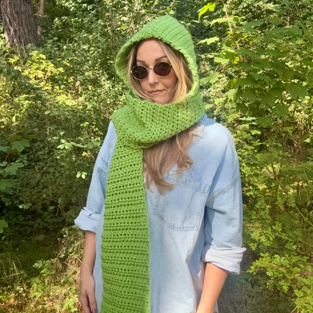 Person wearing a green hood and scarf standing in a forest