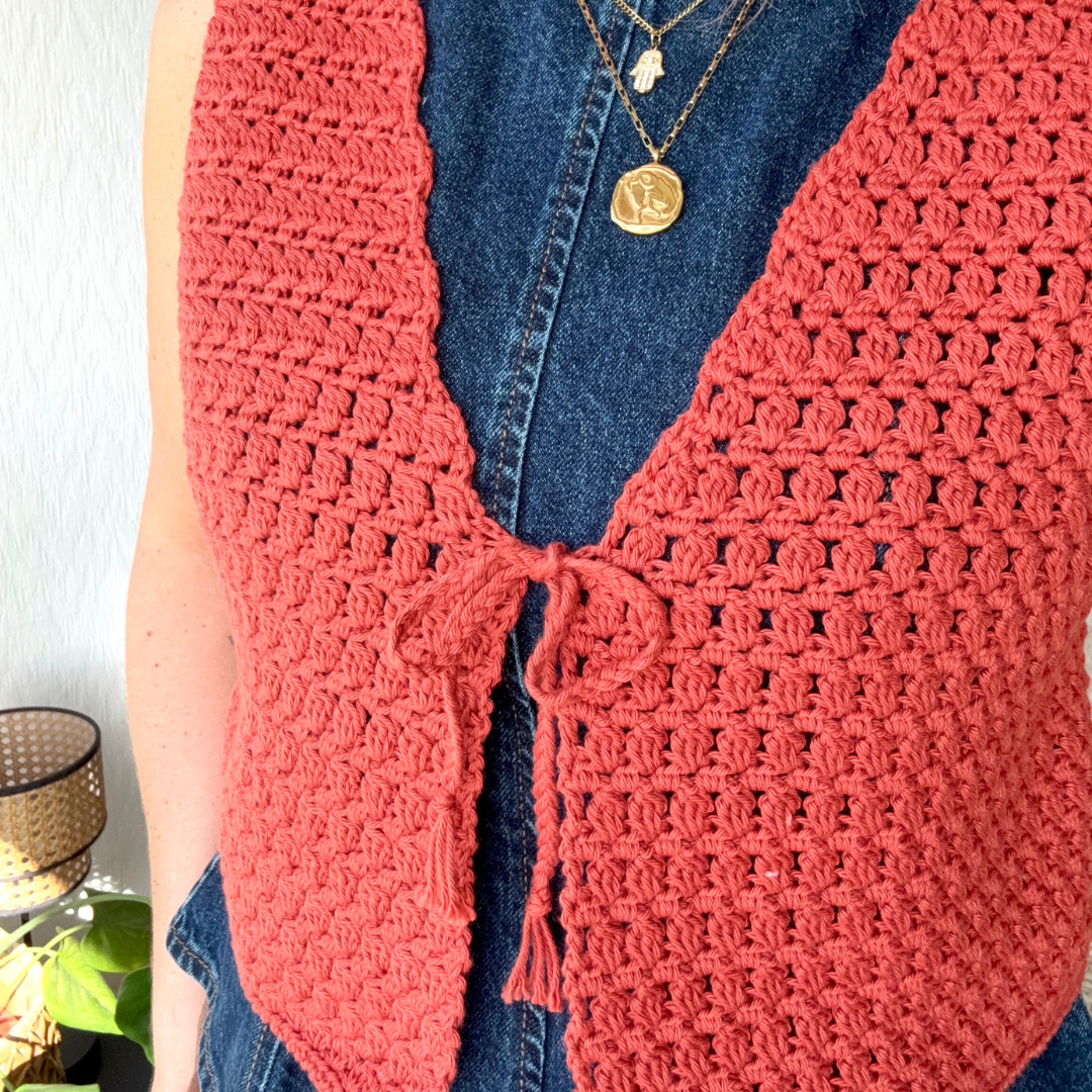 Person wearing a pink crochet cardigan over a blue denim shirt with a white background.