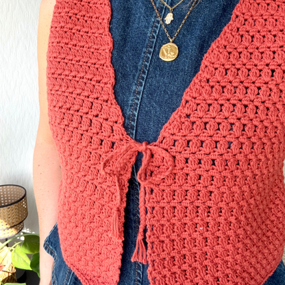 Person wearing a pink crochet cardigan over a blue denim shirt with a white background.