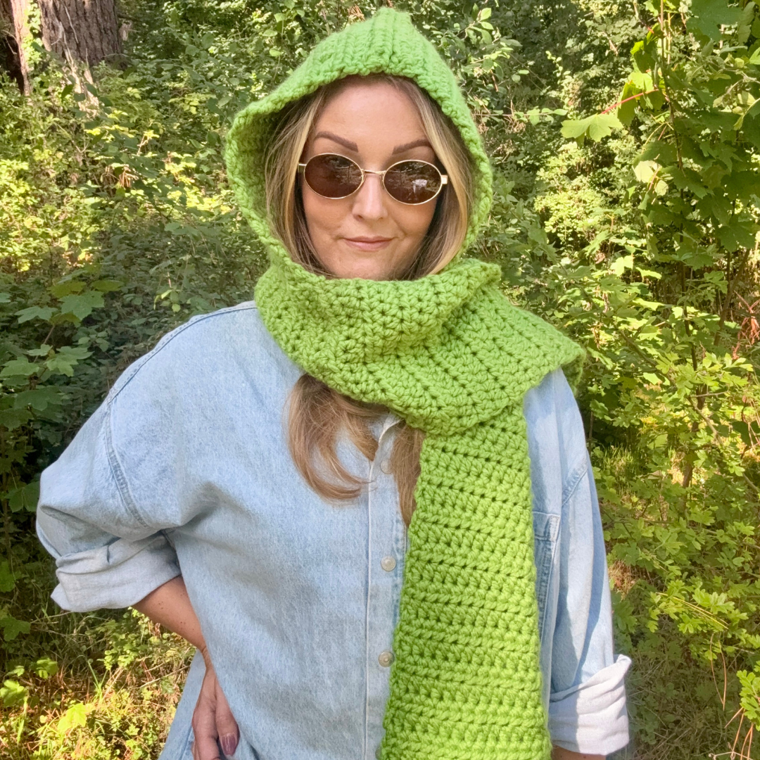 Person wearing a green crochet hood and scarf in a forest setting
