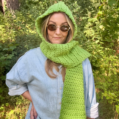 Person wearing a green crochet hood and scarf in a forest setting