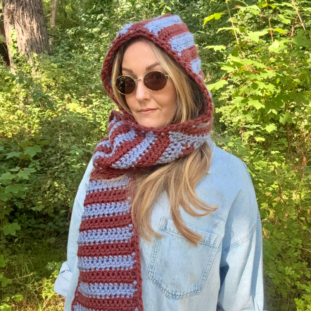 Person wearing a striped crochet hood and scarf in a forest setting